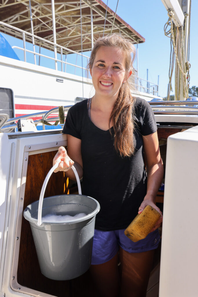 Jenn with a bucket and sponge on the boat about to do some boat maintenance