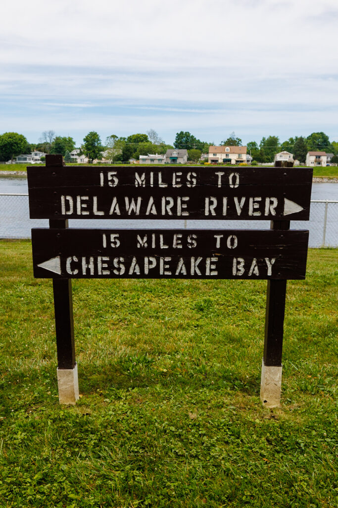 Sign reads: 15 miles to Delaware River pointing right and 15 miles to Chesapeake Bay pointing left.