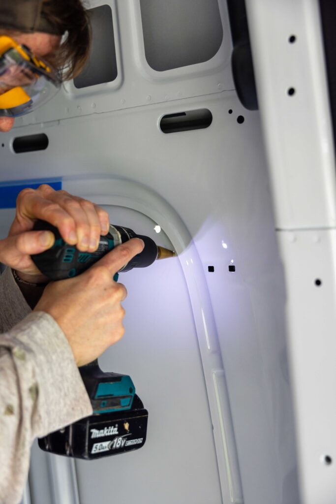 elliot drilling holes into the van with the drill and step bit