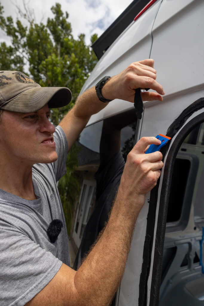 elliot scraping off adhesive from side of van